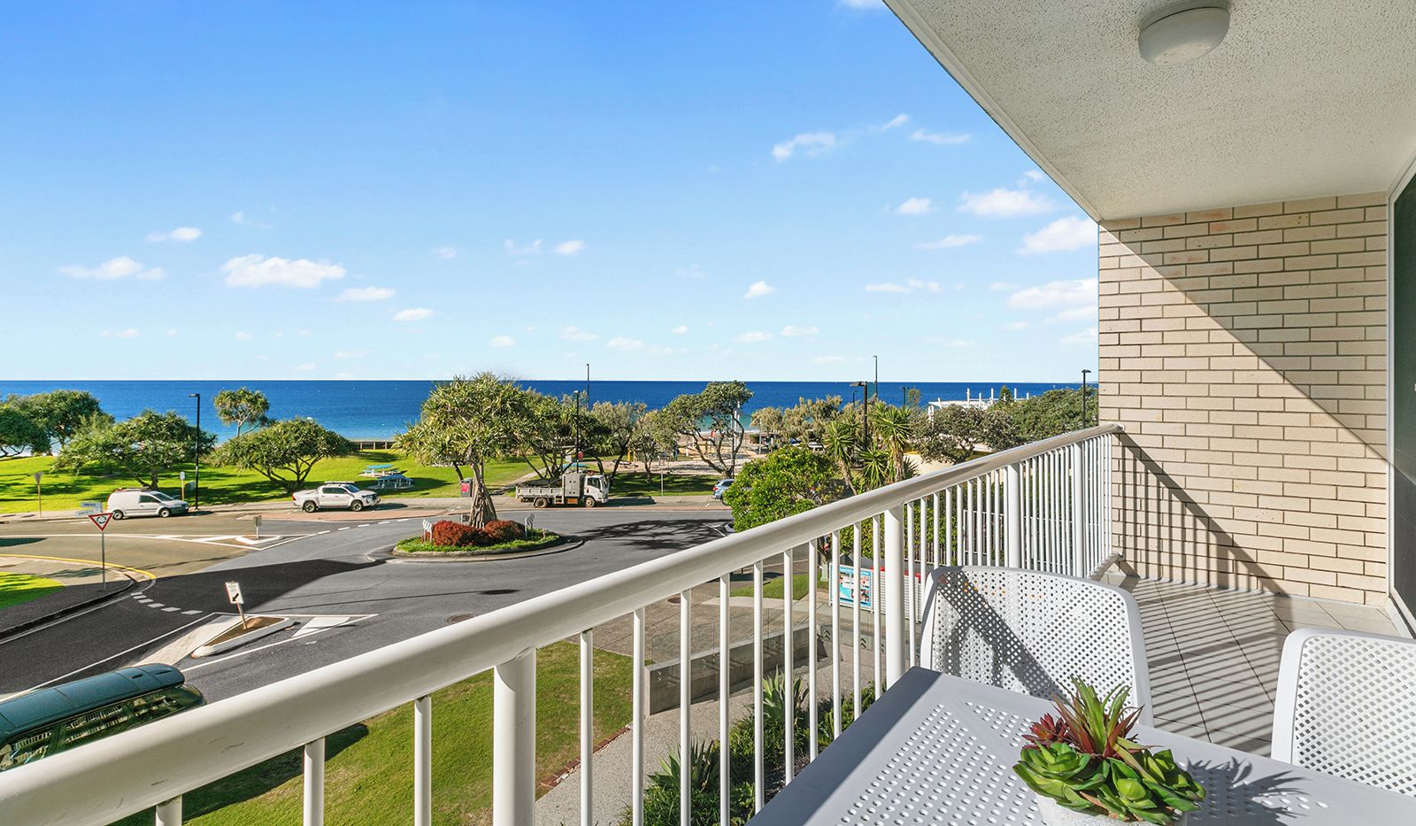 A balcony with a view of the ocean and a parking area.