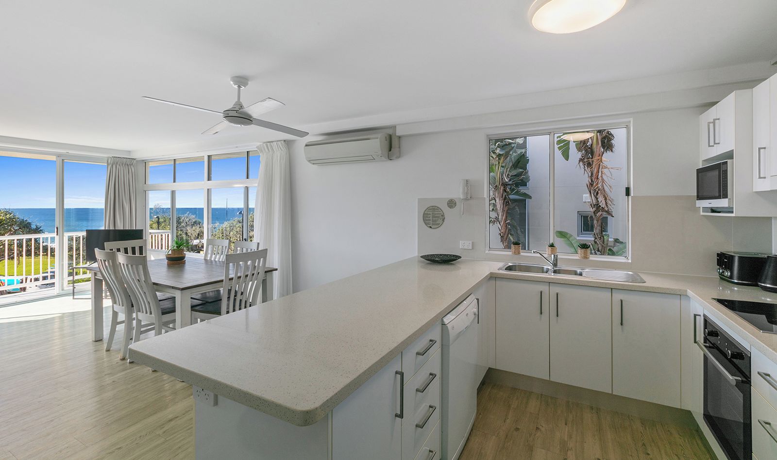 Een moderne keuken met een groot eiland, witte kasten en uitzicht op de oceaan.