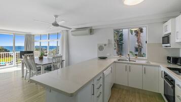 Een moderne keuken met een groot eiland, witte kasten en uitzicht op de oceaan.