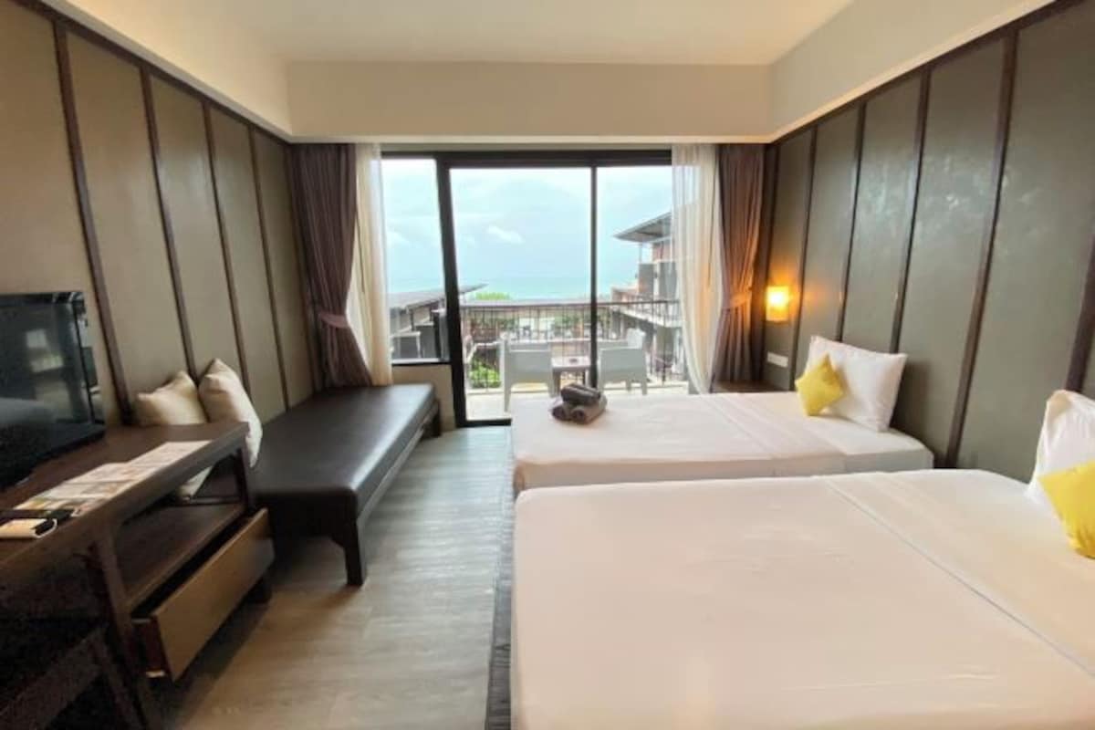 Habitación de hotel con dos camas, televisor, escritorio y vista al océano.