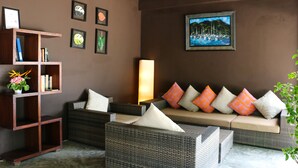 Un rincón acogedor con muebles de mimbre, una estantería y un cuadro de una escena costera.