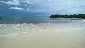Una playa con agua cristalina, orilla arenosa y una isla distante con vegetación.