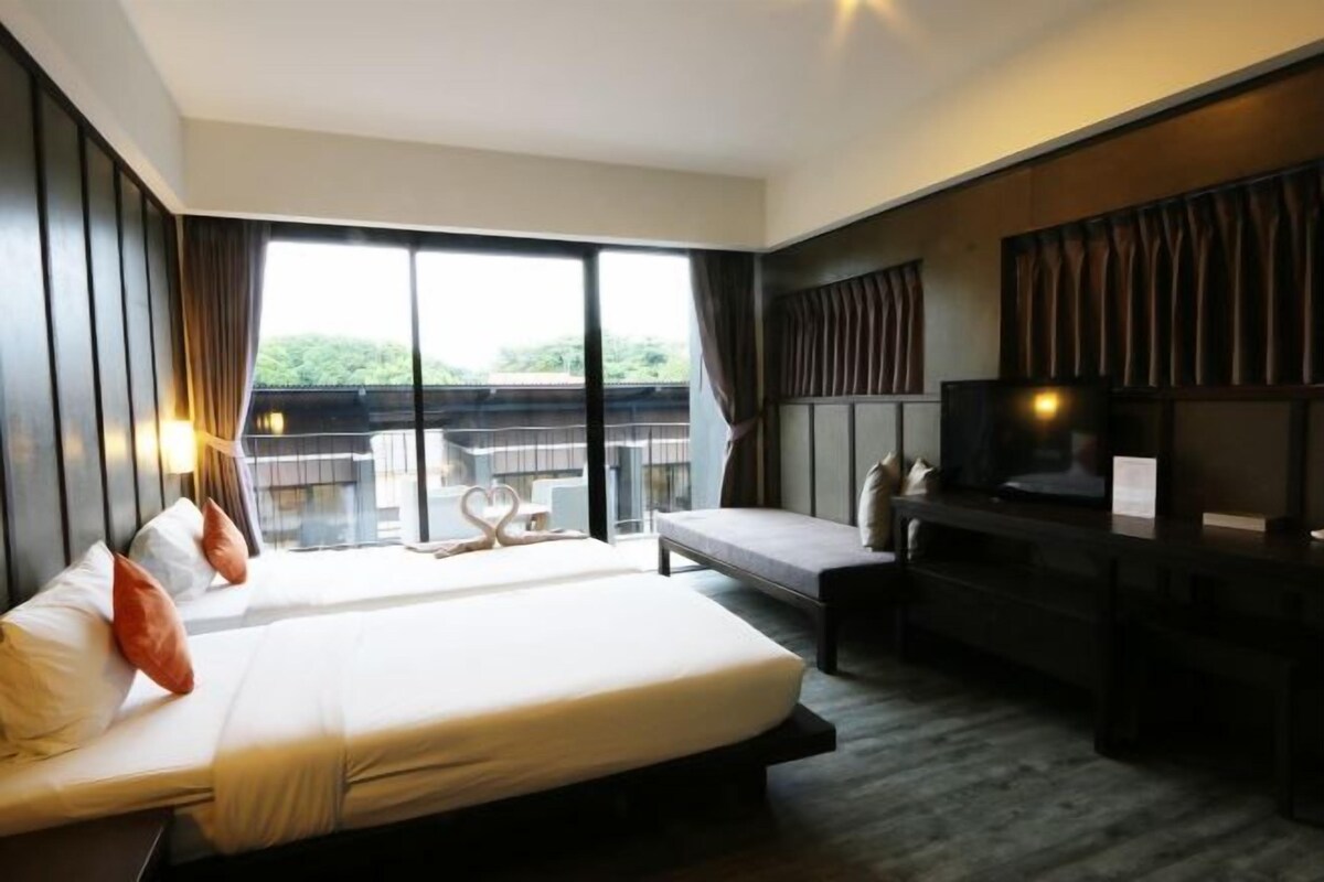 A hotel room with a large bed, a desk with a TV, and a balcony view.