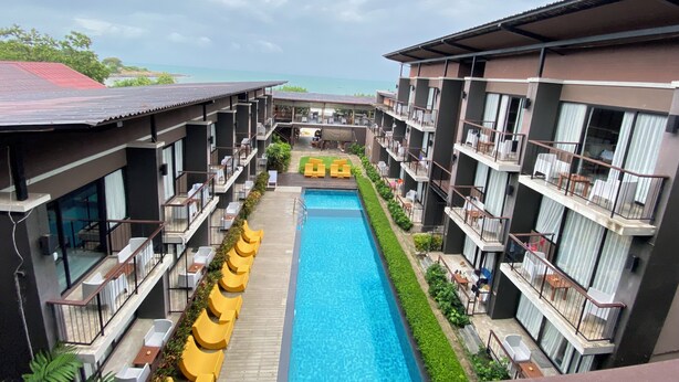 Un hotel con piscina central, varios balcones y vista al mar.