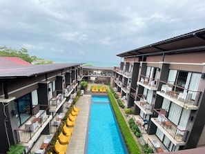 A hotel with a central swimming pool, multiple balconies, and a view of the sea. - LaLune Beach Resort (Rayong)