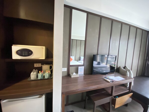A hotel room with a wooden desk, a microwave, a coffee maker, a TV, and a bed with a window view. - LaLune Beach Resort (Rayong)