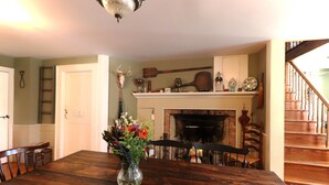A dining area with a wooden table, chairs, a vase of flowers, a fireplace, and a staircase. - The Hann Homestead Inn (Andover)
