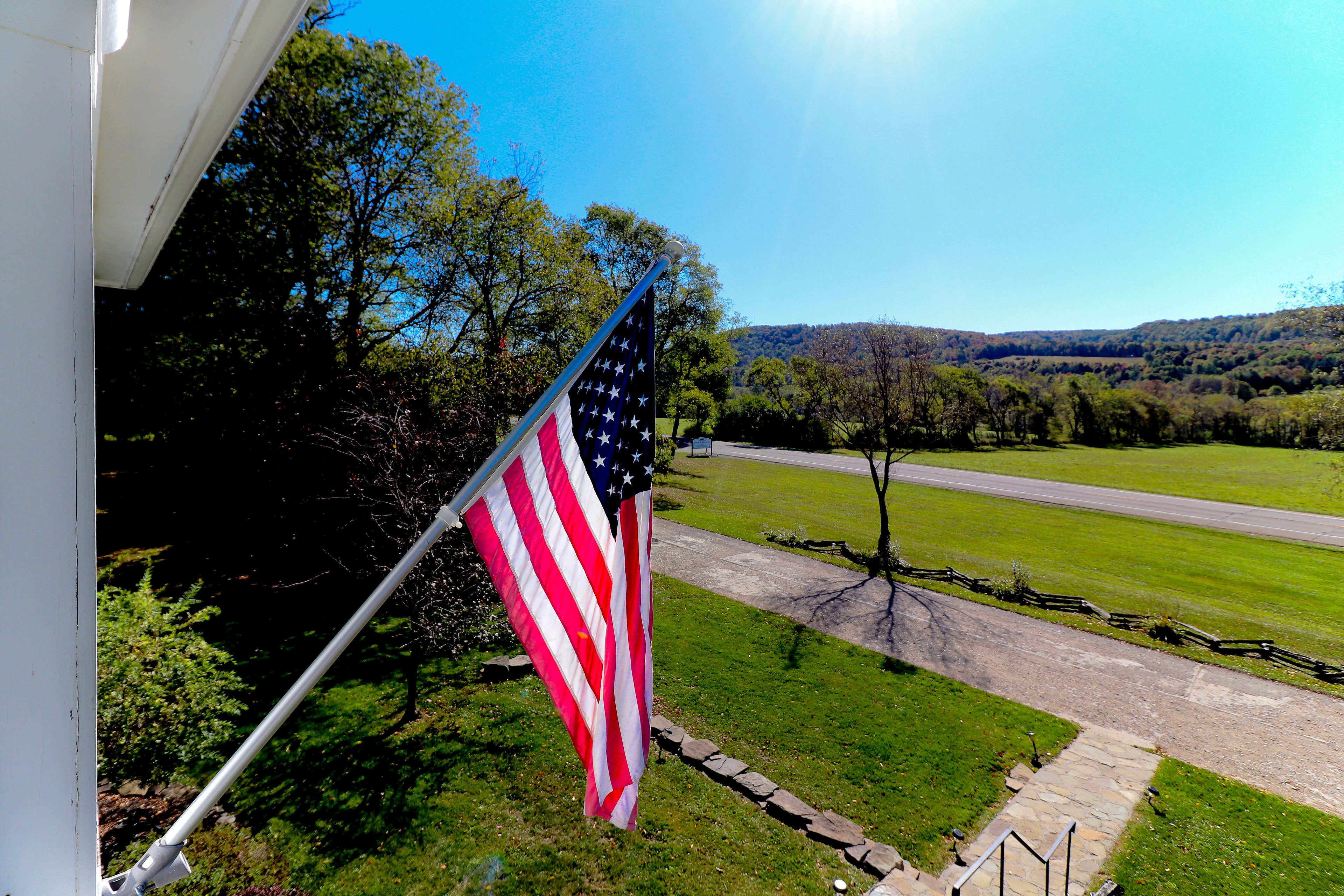 An American flag on a flagpole outside a building with a view of a road and green landscape in the background.
