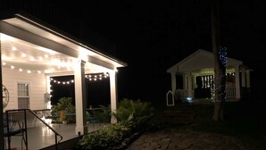 A covered outdoor patio area with string lights, a stone pathway, and a small white building with blue lights. - The Hann Homestead Inn (Andover)