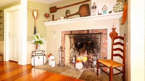 A living room with a fireplace, wooden flooring, a chair, and a shelf with various items. - The Hann Homestead Inn (Andover)