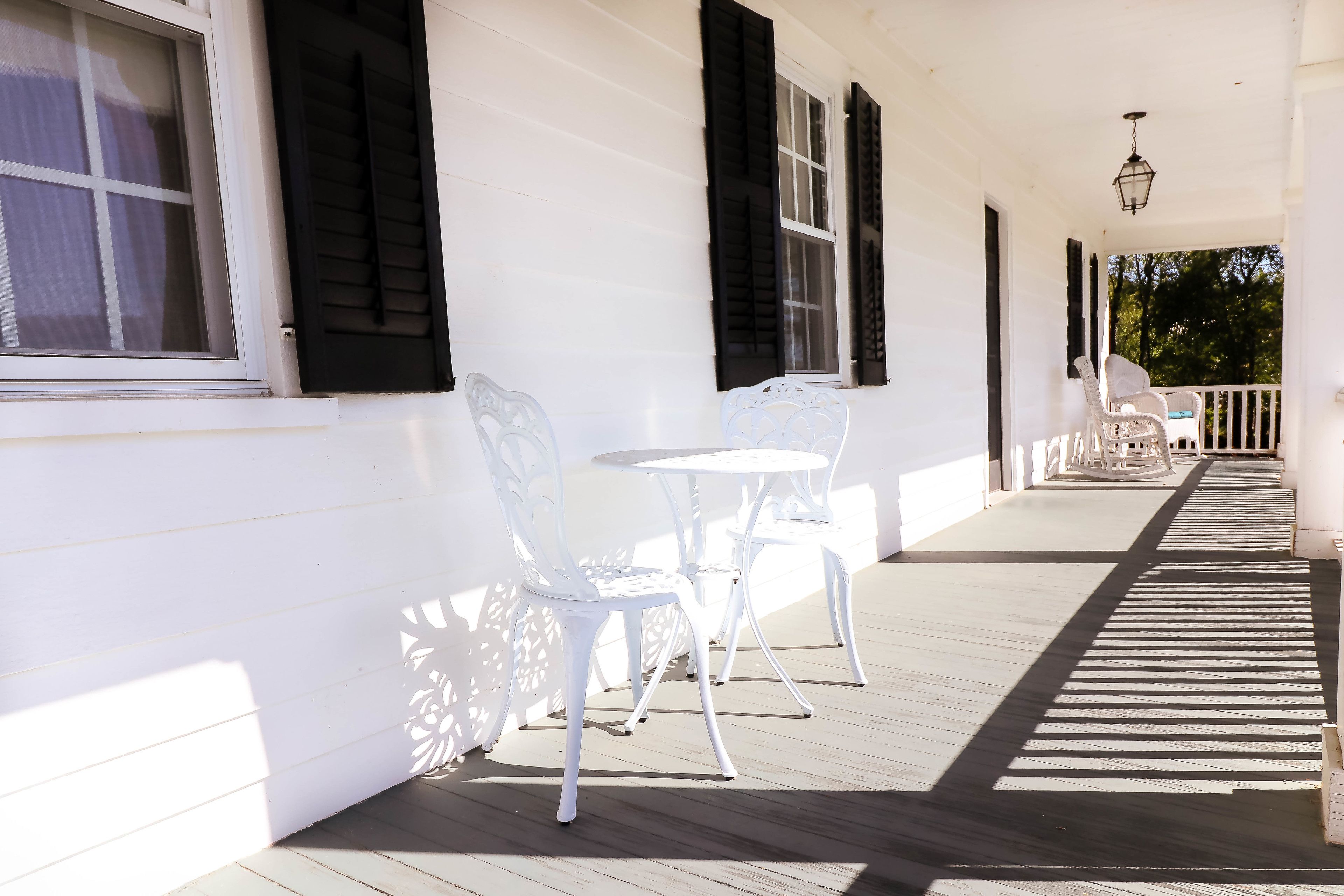 Une véranda couverte avec des chaises et des tables blanches, une balustrade blanche et une lanterne suspendue.