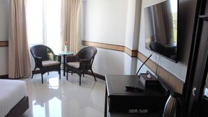 A hotel room with a bed, a TV, a coffee table, two chairs, and a small table with a vase. - Suntara Wellness Resort & Hotel (Chachoengsao)