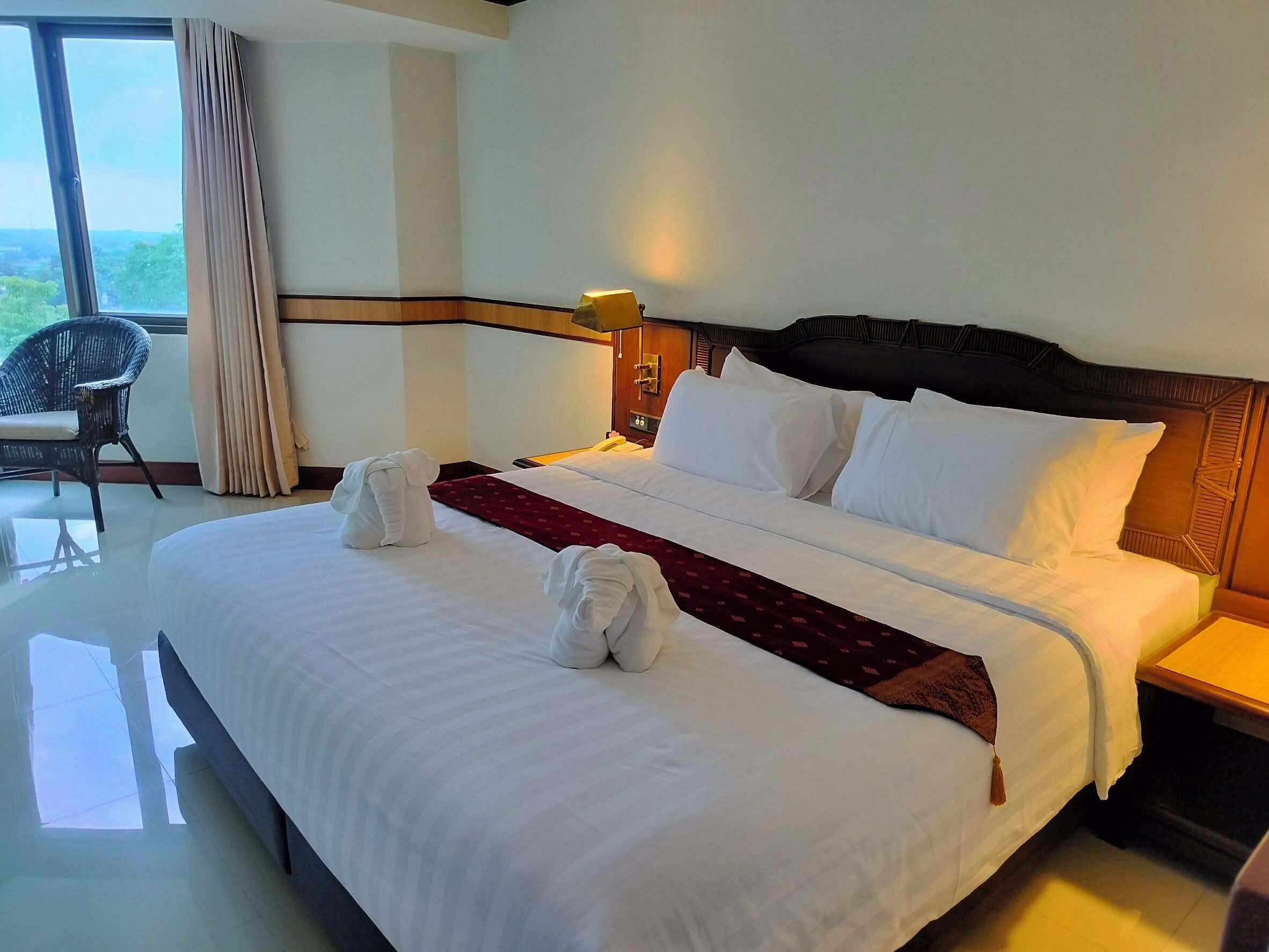 Quarto de hotel com uma cama grande, uma mesa de cabeceira, uma luminária e uma cadeira.