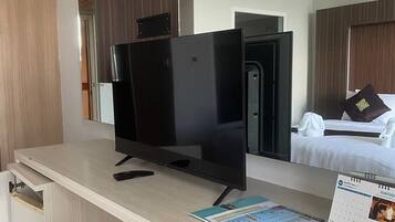 Et hotelværelse med et stort fladskærms-tv på et træskrivebord, en seng med hvide sengetøj og en kalender på væggen.