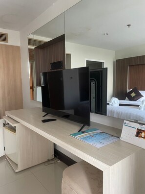 Habitación de hotel con una televisión de pantalla plana grande sobre un escritorio de madera, cama con sábanas blancas y un calendario en la pared.