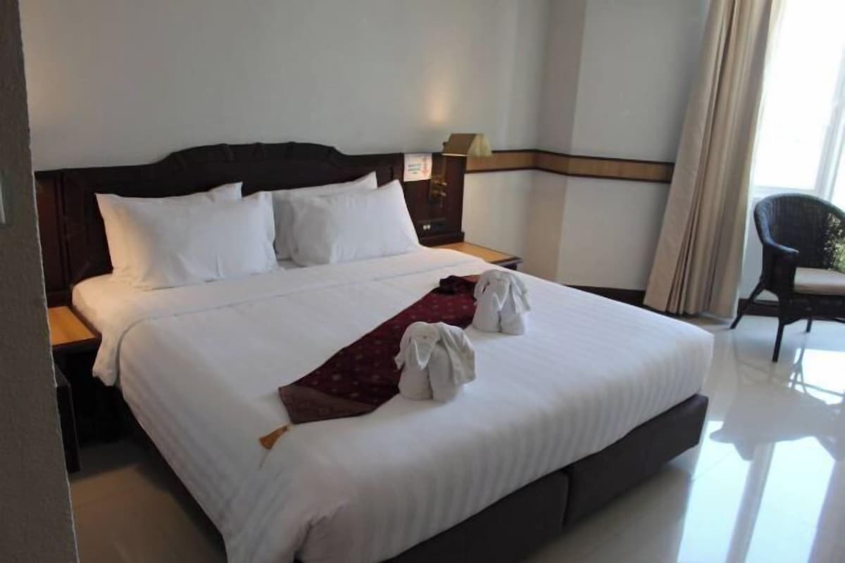 A neatly made bed with white linens, a dark headboard, and two towels placed on the bed.