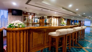 A bar area with wooden bar stools, a counter with a floral arrangement, and a television mounted on the wall. - Suntara Wellness Resort & Hotel (Chachoengsao)