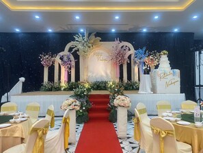 A stage with floral decorations, a red carpet, and a cake with names on it. - Suntara Wellness Resort & Hotel (Chachoengsao)