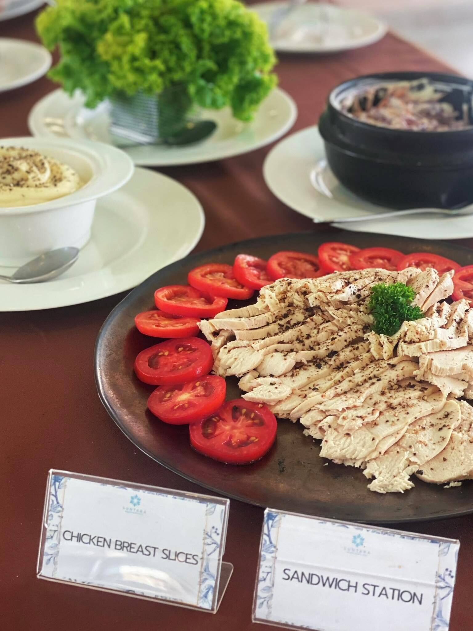 Une table de buffet avec des panneaux indiquant les différents plats, notamment des « tranches de poulet » et un « coin sandwich ».