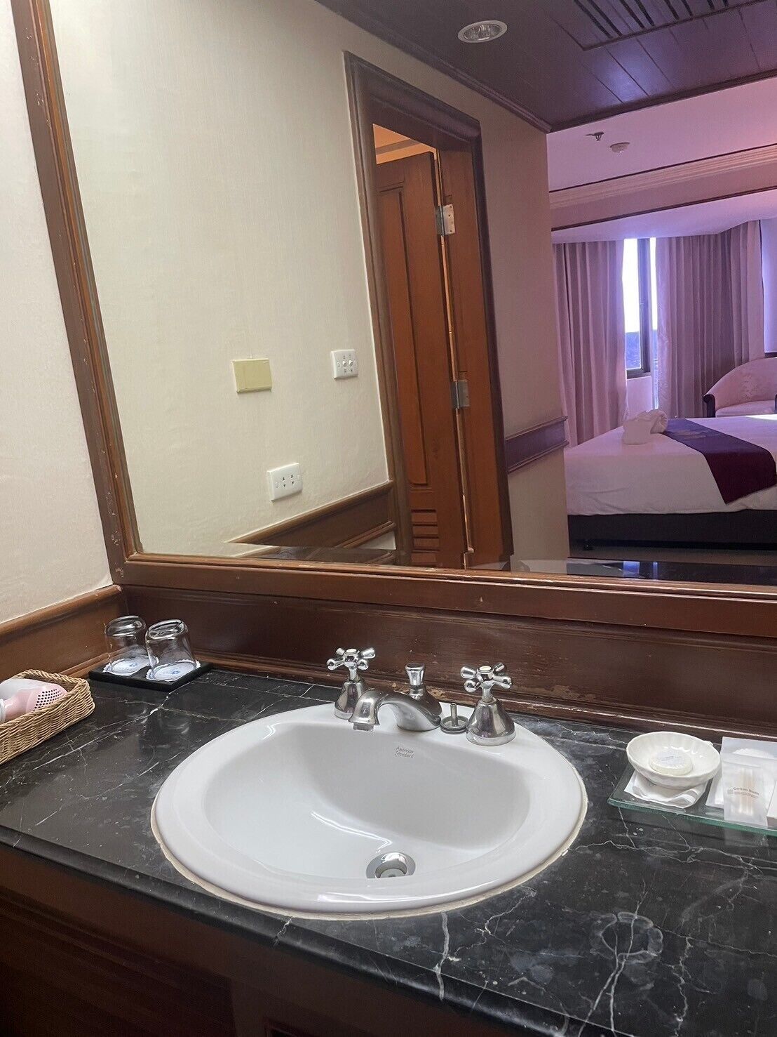 Un baño de hotel con un espejo grande, un lavabo con dos grifos y una ventana pequeña.