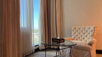 A room with a glass table, a tufted armchair, and a view through sheer curtains.