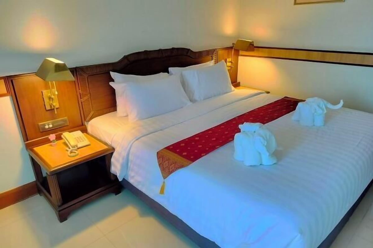 A hotel room with a large bed, a nightstand with a lamp, and a telephone.