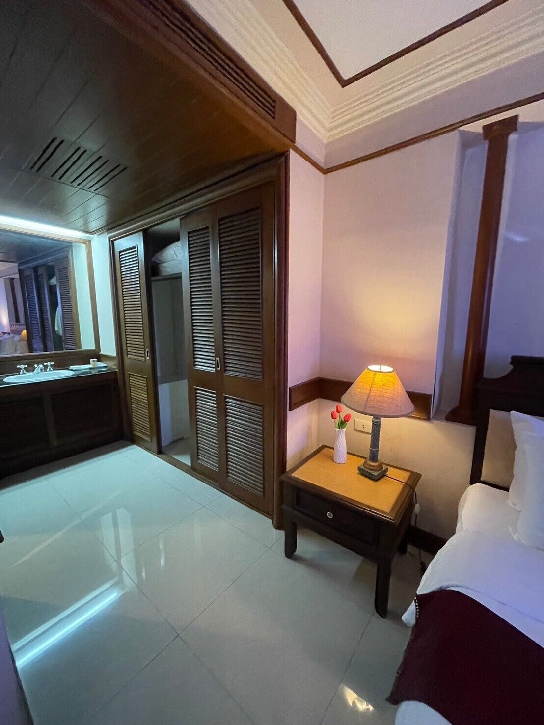 Una habitación de hotel con cama, mesita de noche, lámpara y espejo.