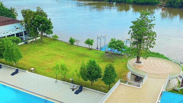 A swimming pool with a deck, a covered seating area, and a view of a river and greenery. - Suntara Wellness Resort & Hotel (Chachoengsao)