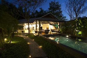 Área externa bem iluminada com piscina, assentos e uma estrutura coberta.