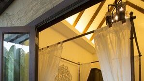 Una cama con dosel adornada con ropa de cama blanca, un cabecero de madera y una mesita de noche con lámpara.
