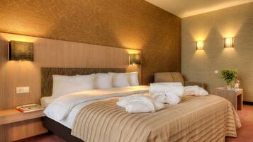 A modern hotel room with a large bed, a bedside table with a book, and two wall-mounted lamps.