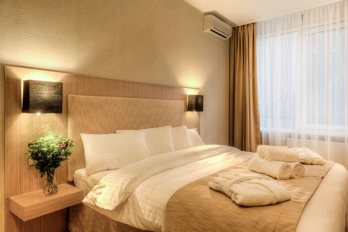 A hotel room with a large bed, a nightstand with a vase of flowers, and a window with curtains.