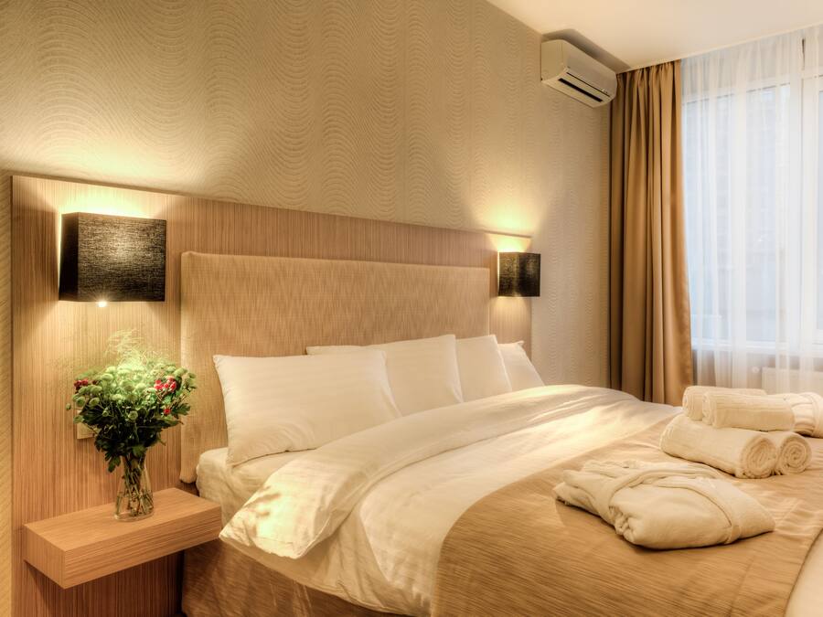 A hotel room with a large bed, a nightstand with a vase of flowers, and a window with curtains.