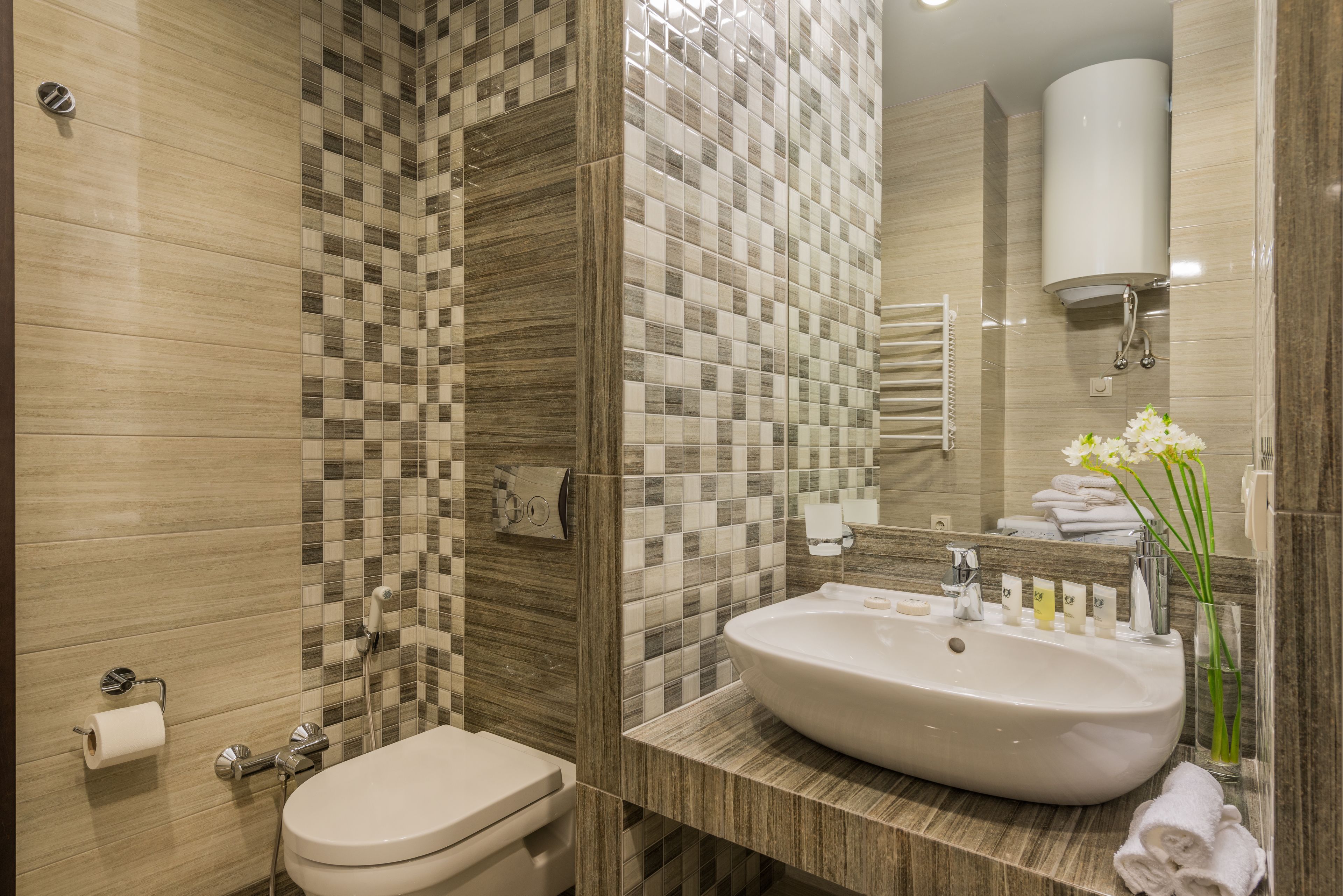 A modern bathroom with a tiled shower wall, a sink with toiletries, and a toilet.