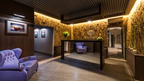 Un espace d’accueil avec un mur en bois, un tableau encadré, un canapé moelleux, une petite table et une chaise.