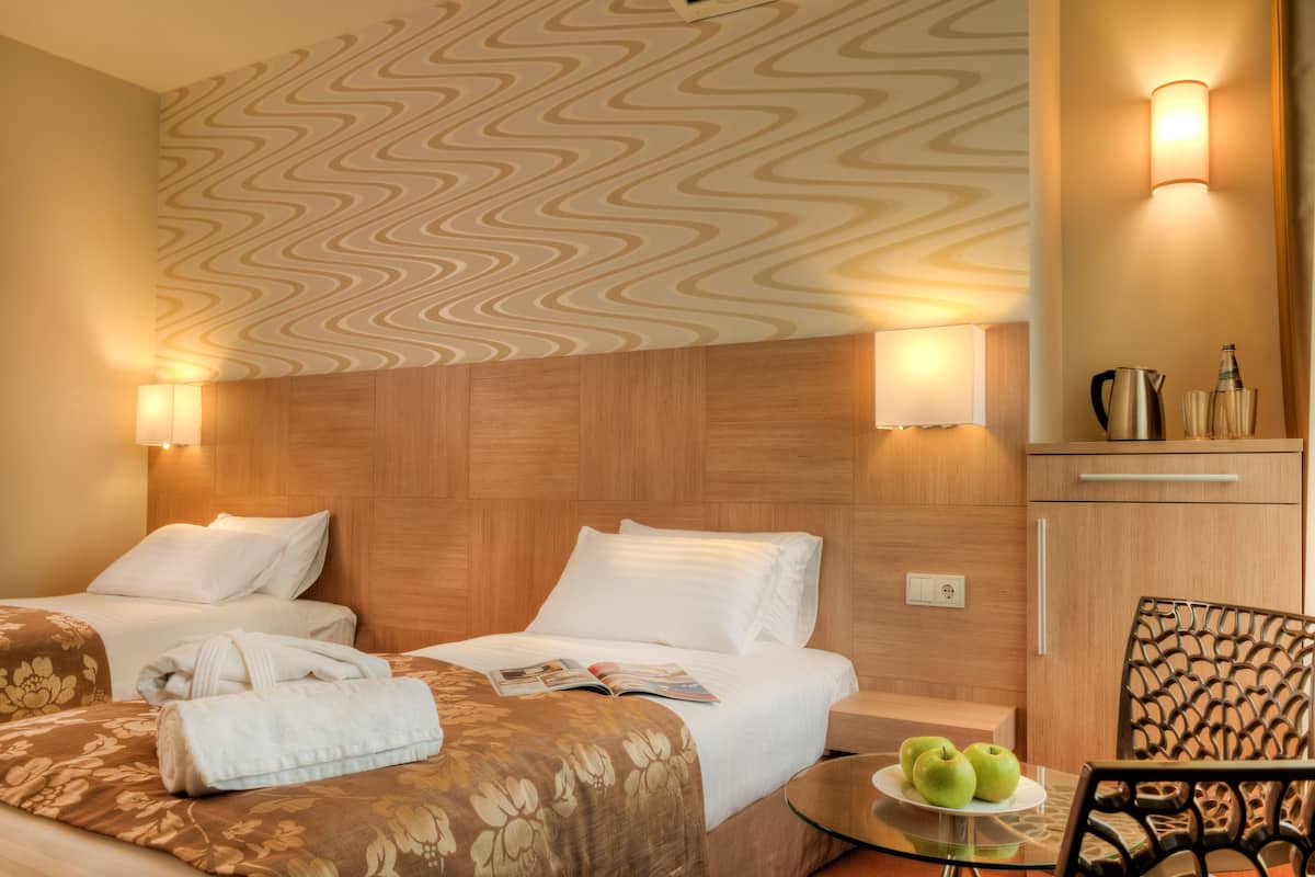 A hotel room with two beds, a wooden headboard, a wall-mounted light, a small table with apples, and a chair.