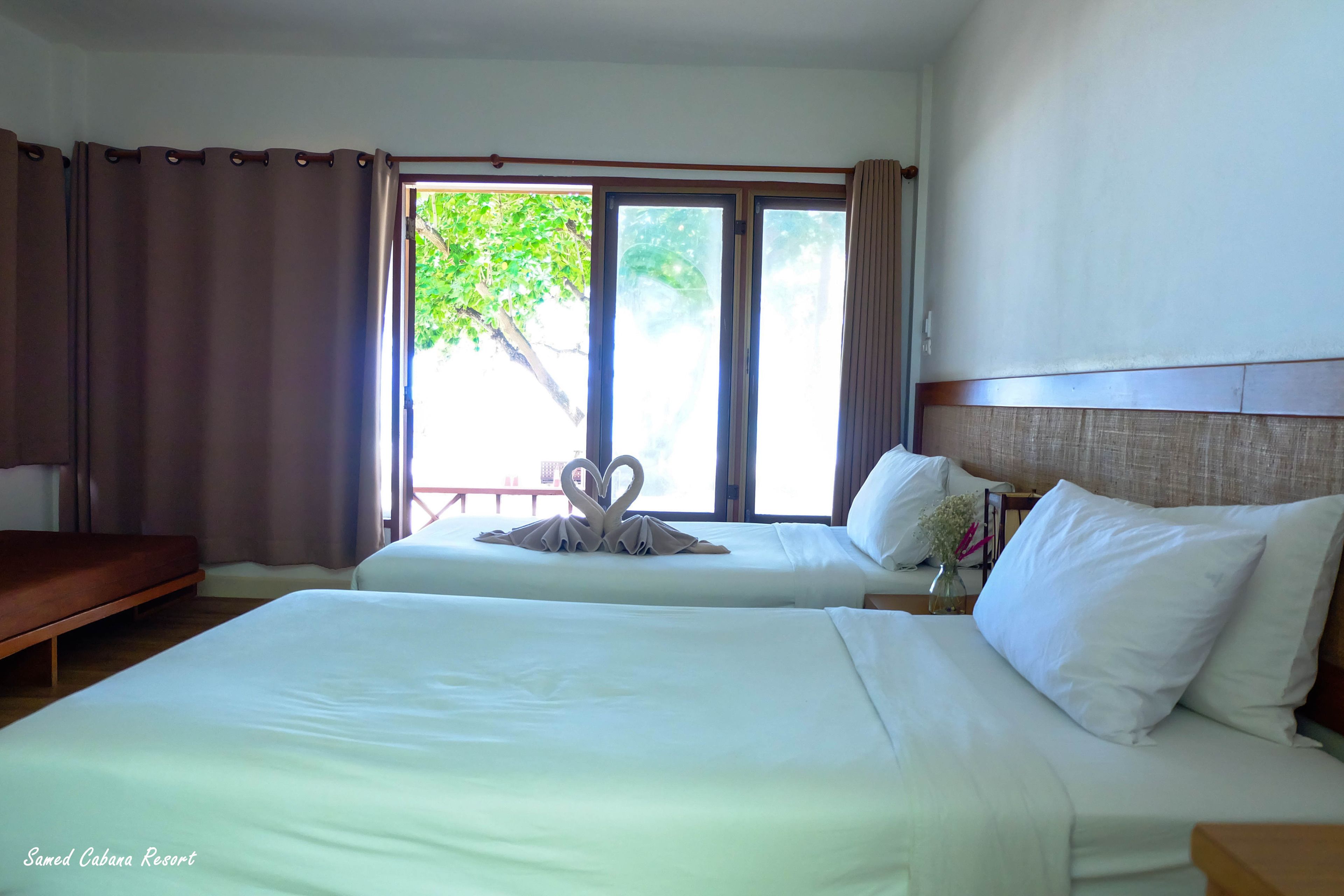 A hotel room with two beds, a wooden bench, and a window with curtains.