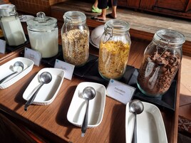 Un bufé con recipientes etiquetados de yogur, copos de maíz y cereal de chocolate.