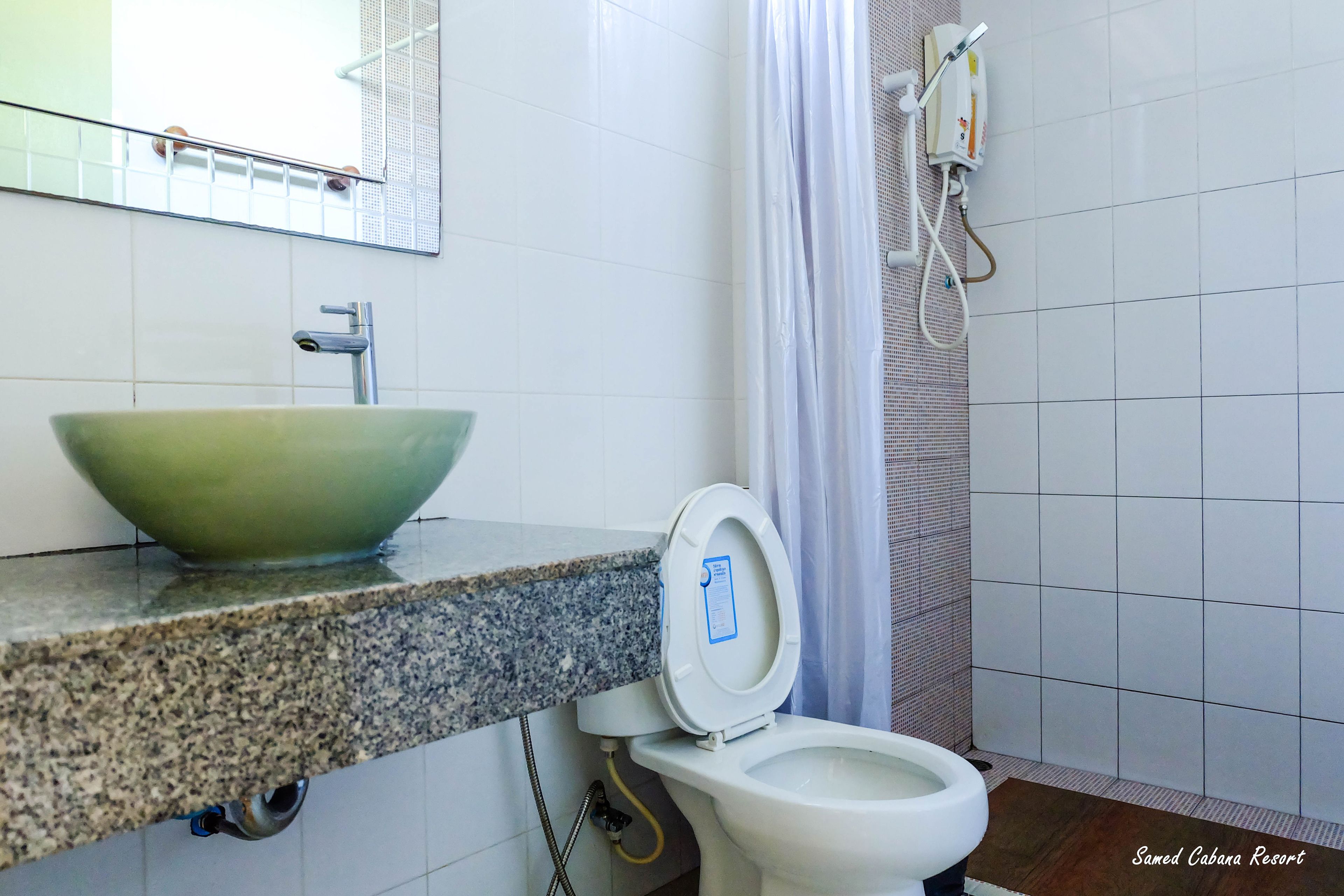 A bathroom with a granite countertop, a green ceramic sink, a white toilet, and a shower with a curtain.