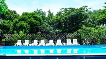A swimming pool with white lounge chairs and a lush green backdrop.