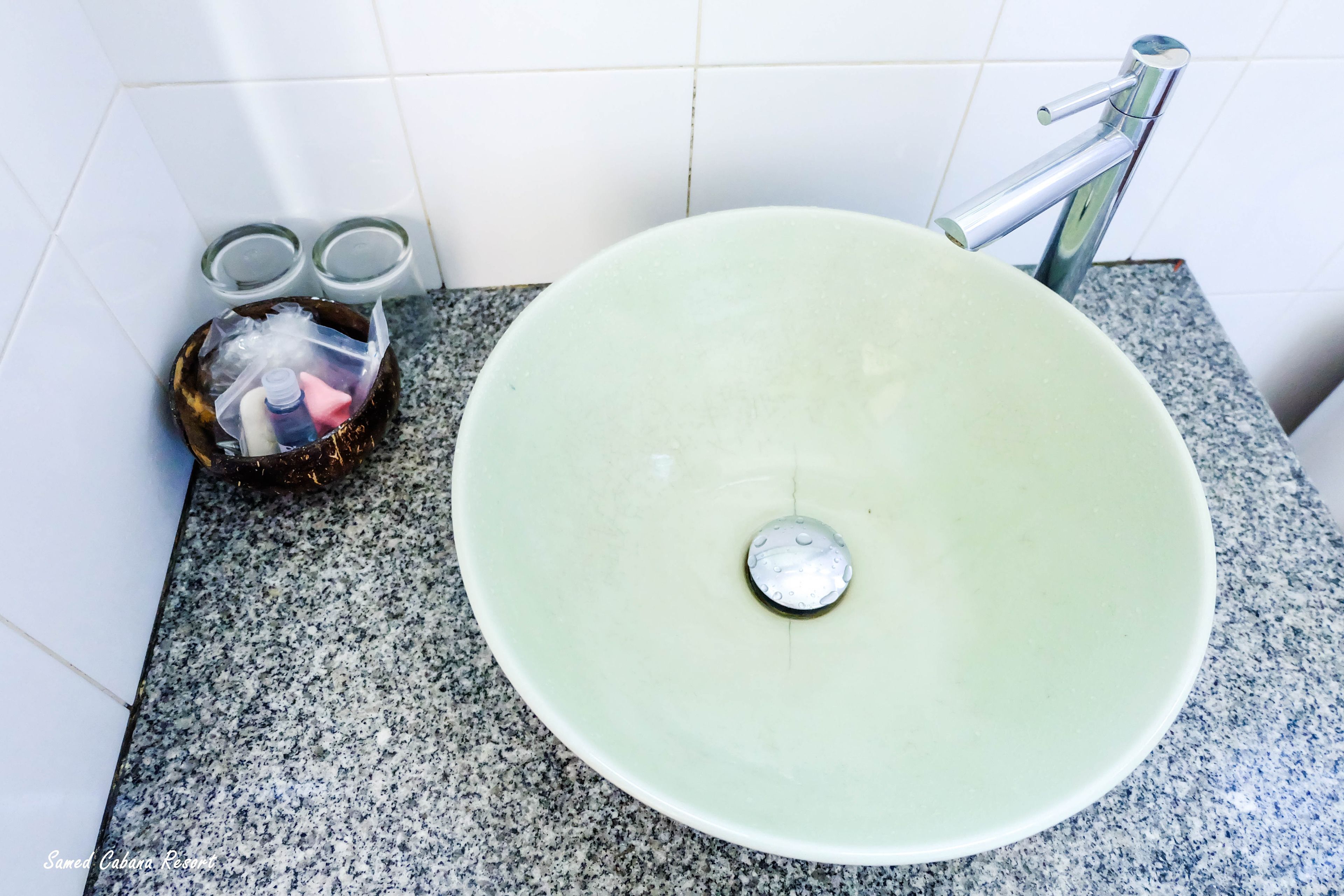 Un baño con un lavamanos verde, encimera de granito y dos cubos de basura con tapa de vidrio.