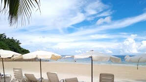 A beach with white lounge chairs and umbrellas, a palm tree, and a clear sky. - Samed Cabana Resort (Rayong)