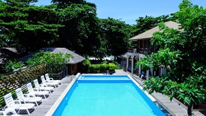 A swimming pool with lounge chairs, surrounded by greenery and a building with a tiled roof. - Samed Cabana Resort (Rayong)