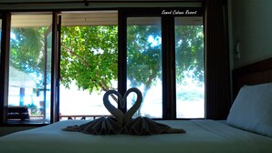 A hotel room with a bed, a heart-shaped towel decoration, and a view of trees through the window. - Samed Cabana Resort (Rayong)