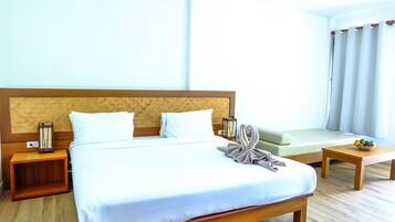 A hotel room with a large bed, a wooden headboard, a bedside table with a lamp, a small table with fruit, and a sofa.
