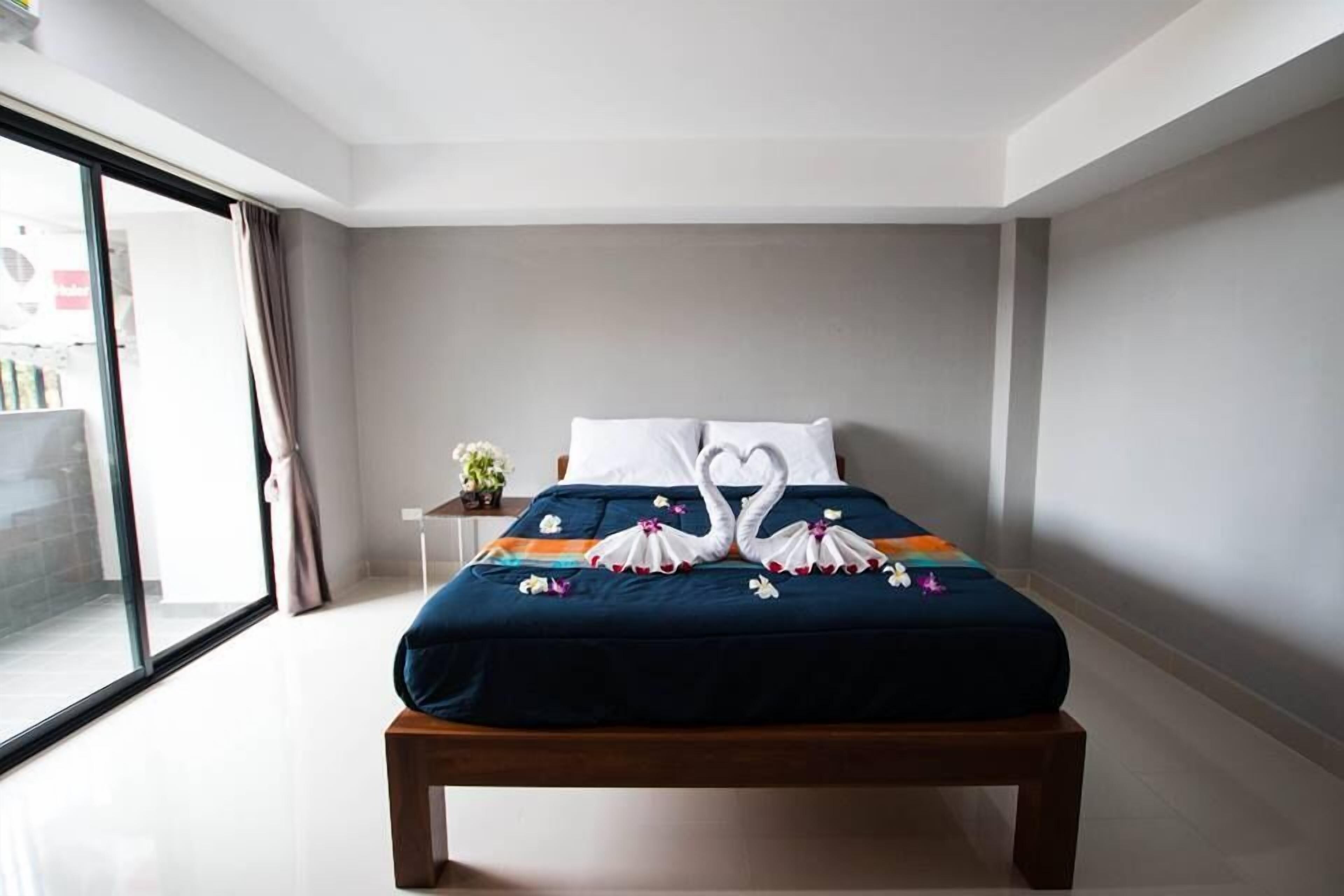 Une chambre d’hôtel avec un lit, une table de chevet, une plante en pot et une vue sur l’extérieur par une grande fenêtre.