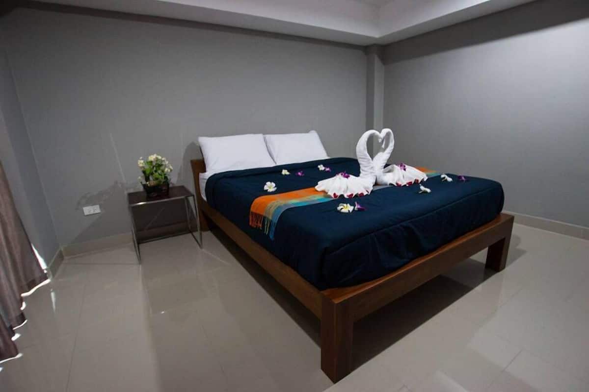 A neatly made bed with a blue bedspread, white pillows, and a heart-shaped towel decoration.