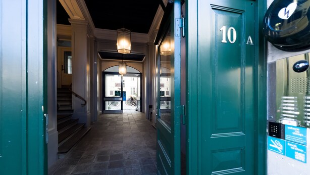 Un pasillo con una puerta verde identificada con '10A', una escalera y vistas a la calle.