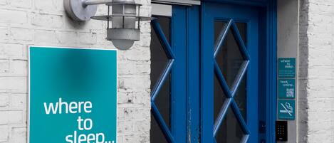 Une porte bleue avec une pancarte indiquant « où dormir… » et un luminaire au-dessus.