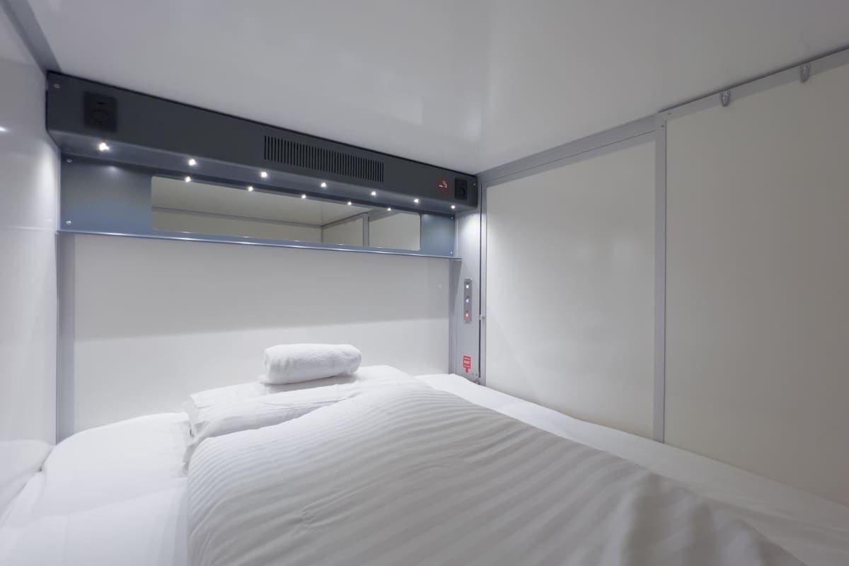 A hotel room with a bed, a large mirror, and a control panel.